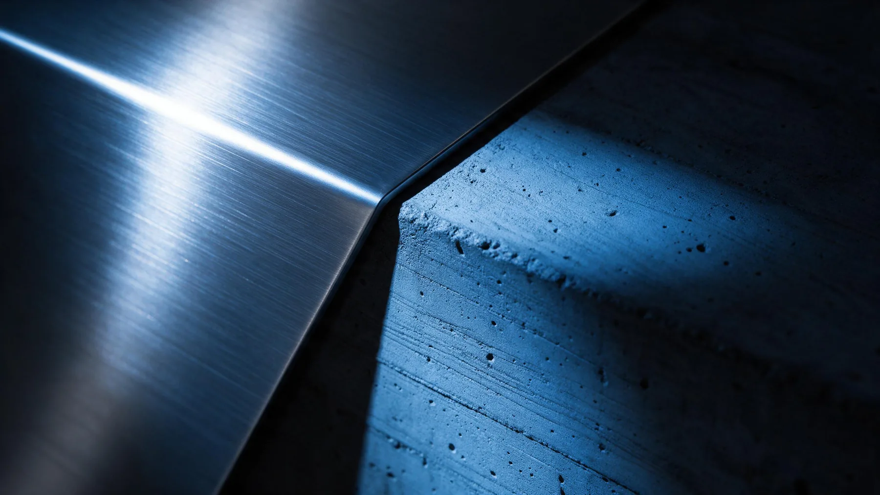 Brushed steel and raw concrete meeting along a sharp diagonal edge under cool blue light